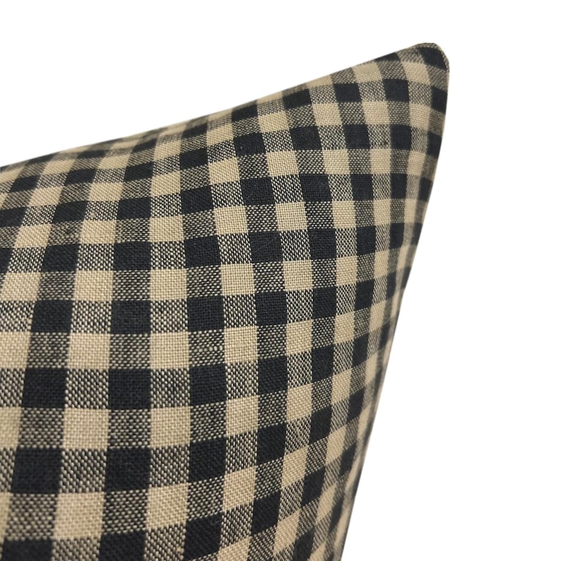K&ouml;nnte beinhalten: Ein schwarzer und beigefarbener Gingham-Kissenbezug. Der Kissenbezug ist aus einem weichen, gewebten Stoff mit einem karierten Muster.