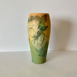 May include: A ceramic vase with a green and yellow gradient glaze. The vase is decorated with a floral pattern of white roses and leaves.