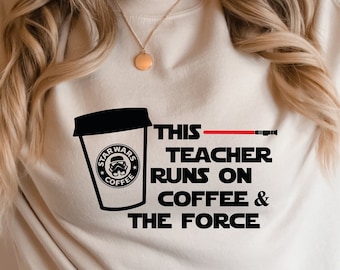 May include: Beige sweatshirt with a black graphic of a coffee cup with the Star Wars logo and the text "THIS TEACHER RUNS ON COFFEE & THE FORCE". The design includes a red lightsaber. The sweatshirt is a neutral color.