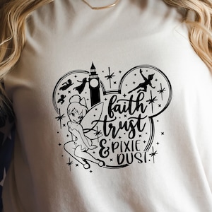 May include: A white t-shirt with a black graphic of Tinkerbell flying in a Mickey Mouse ear shape. The graphic also includes the text "faith trust & pixie dust".