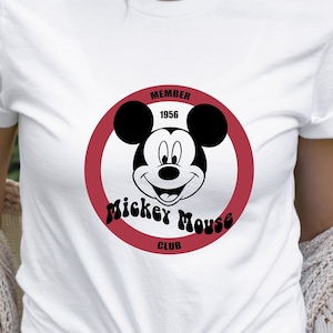 May include: White t-shirt with a red circle and black Mickey Mouse head graphic. The circle has the text "Member 1956 Mickey Mouse Club" around it.