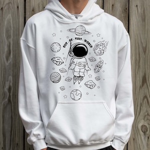 May include: White hoodie with a black and white illustration of an astronaut in space. The astronaut is surrounded by planets, stars, and a rocket. The text "OUT OF THIS WORLD" is written around the astronaut.
