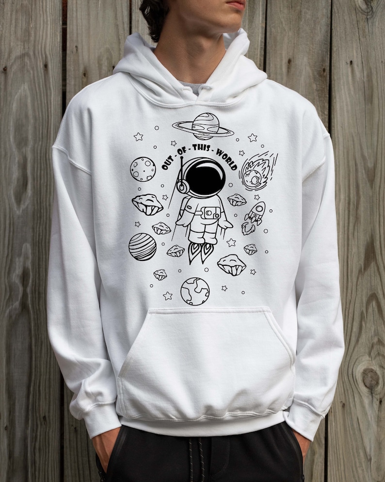 May include: White hoodie with a black and white illustration of an astronaut in space. The astronaut is surrounded by planets, stars, and a rocket. The text "OUT OF THIS WORLD" is written around the astronaut.