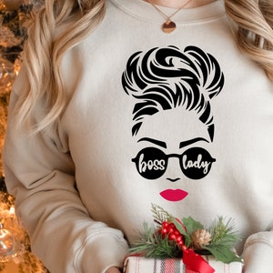 May include: A white sweatshirt with a black graphic of a woman with a bun, sunglasses, and the text "boss lady".