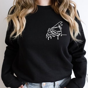 May include: A black sweatshirt with a white line drawing of a person playing a grand piano.