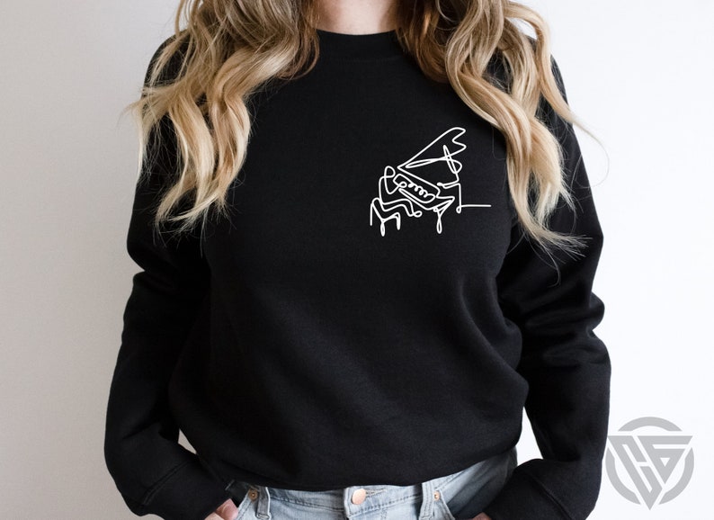 May include: A black sweatshirt with a white line drawing of a person playing a grand piano.