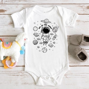 May include: White baby onesie with a black and white illustration of an astronaut in space. The text "OUT OF THIS WORLD" is written around the astronaut.