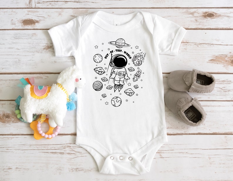May include: White baby onesie with a black and white illustration of an astronaut in space. The text "OUT OF THIS WORLD" is written around the astronaut.