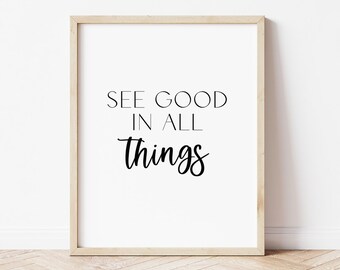 May include: A framed print with the words "SEE GOOD IN ALL THINGS" in black lettering on a white background. The frame is a light wood color, and the print is displayed against a white wall and a wooden floor.