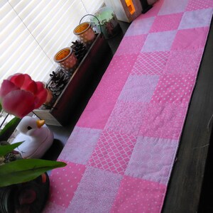 May include: Pink and white patchwork table runner with a variety of patterns, including polka dots, diamonds, and floral designs.