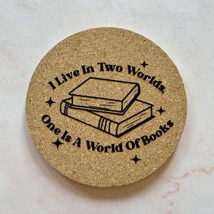 K&ouml;nnte beinhalten: Ein runder Korkuntersetzer mit dem Text "Ich lebe in zwei Welten, eine ist eine Welt der B&uuml;cher" und einer Schwarzwei&szlig;illustration eines B&uuml;cherstapels.