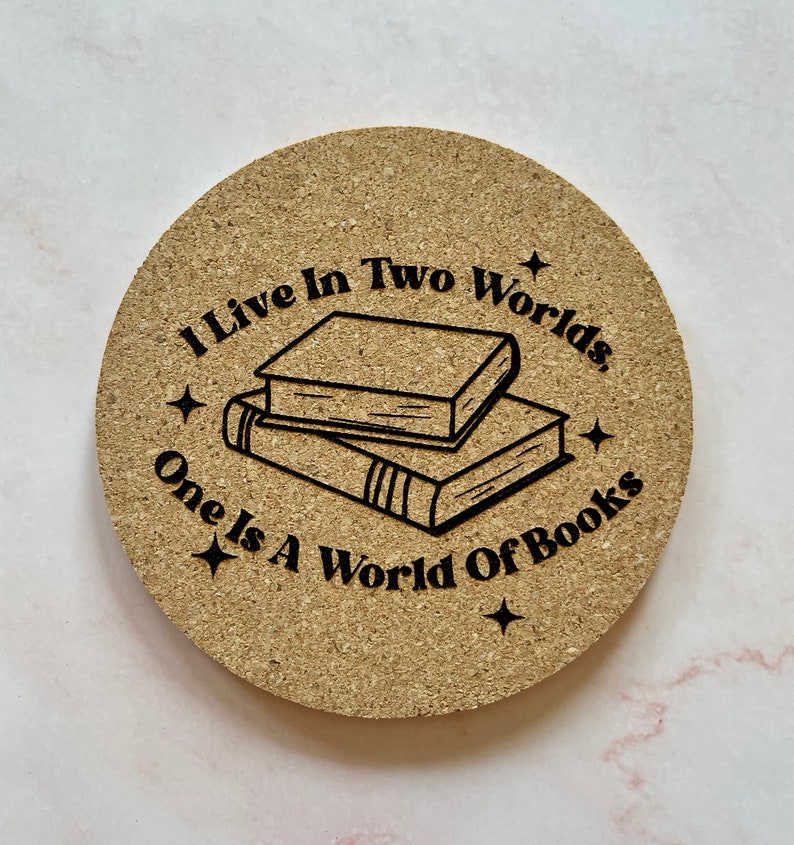 K&ouml;nnte beinhalten: Ein runder Korkuntersetzer mit dem Text "Ich lebe in zwei Welten, eine ist eine Welt der B&uuml;cher" und einer Schwarzwei&szlig;illustration eines B&uuml;cherstapels.
