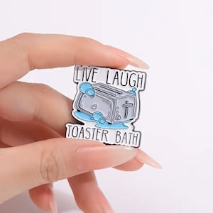 May include: A white enamel pin with a cartoon illustration of a toaster in a bubble bath. The text "Live Laugh Toaster Bath" is printed around the toaster.
