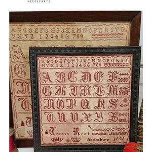 May include: A framed cross-stitch sampler with a red alphabet, numbers, and the words "Teresa Real" and "Octubre 1898".