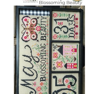 May include: A cross-stitch sampler with a black frame and a beige background. The sampler is divided into four sections. The top left section features a butterfly with pink and red wings. The top right section features the text "31 Days". The bottom left section features the text "May" and the text "Blossoming Beauty". The bottom right section features the number "26".