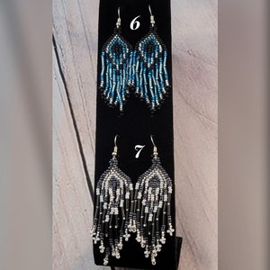 May include: Two pairs of beaded earrings, one pair is blue, black, and silver, the other pair is white, black, and silver. The earrings are labeled with the numbers 6 and 7.