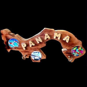 May include: Wooden key holder shaped like the outline of Panama with the word "PANAMA" in gold letters. The key holder has three hooks and three round magnets with images of Panama.