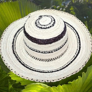 May include: A white straw hat with black and brown woven bands. The hat has a wide brim and a tall crown.