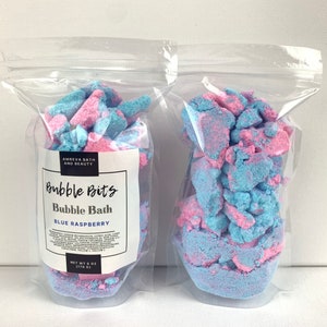 May include: Two clear plastic bags filled with blue and pink bubble bath bits. The bag on the left has a label that reads "Bubble Bits Bubble Bath Blue Raspberry Net Wt 6 oz (170 g)"