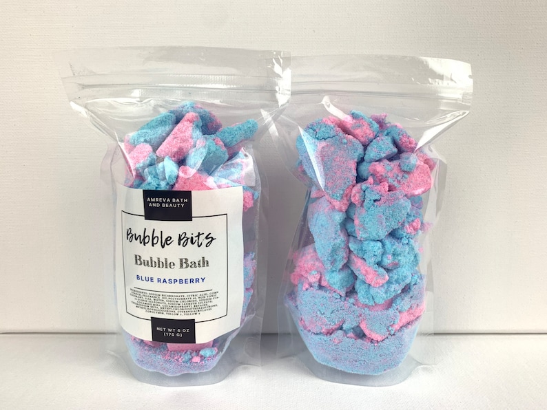 May include: Two clear plastic bags filled with blue and pink bubble bath bits. The bag on the left has a label that reads "Bubble Bits Bubble Bath Blue Raspberry Net Wt 6 oz (170 g)"