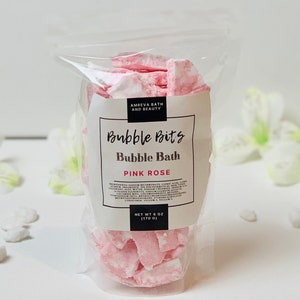 May include: A clear plastic bag filled with pink and white bubble bath bits. The label reads "Bubble Bits Bubble Bath Pink Rose" and "Net Wt 6 oz (170 g)".