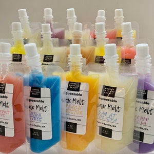 May include: An assortment of squeezeable wax melts in clear pouches, each with a white cap. The pouches contain colorful wax in shades of pink, blue, yellow, and purple. Each pouch has a label with the scent name and brand information.