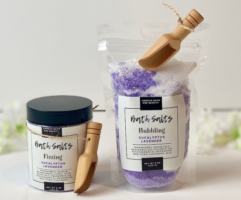 Pode incluir: Dois frascos de sais de banho, um com sal de banho de eucalipto e lavanda efervescente roxo e branco e o outro com sal de banho de eucalipto e lavanda efervescente branco e roxo. Ambos os frascos t&ecirc;m uma pequena concha de madeira.