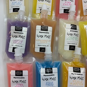 May include: An assortment of squeezable wax melts in various colors and scents, including "Day at the Spa," "Lemon Pound," and "Pink Sugar." Each pouch is labeled with the scent name and brand information. The pouches are 4 oz (113 g) each.