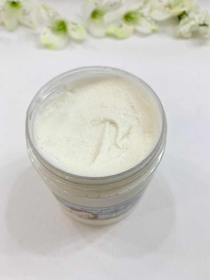 May include: A white jar of body butter with a white lid. The jar is filled with a white, creamy product. The jar has a label on the bottom that says "Sweet Pea and White Tea Body Butter".
