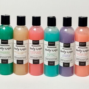May include: Eight clear plastic bottles of body wash with black lids and labels. The labels have the text "Moisturizing Body Wash" and list different scents, including Rose Water, Cucumber Watermelon, Vanilla &  Liquorice Cream, Raspberry White Mint, Coconut Key Lime, Lavender Oatmilk, Tropical Fruit Sugar Cane, and Milk & Honey.