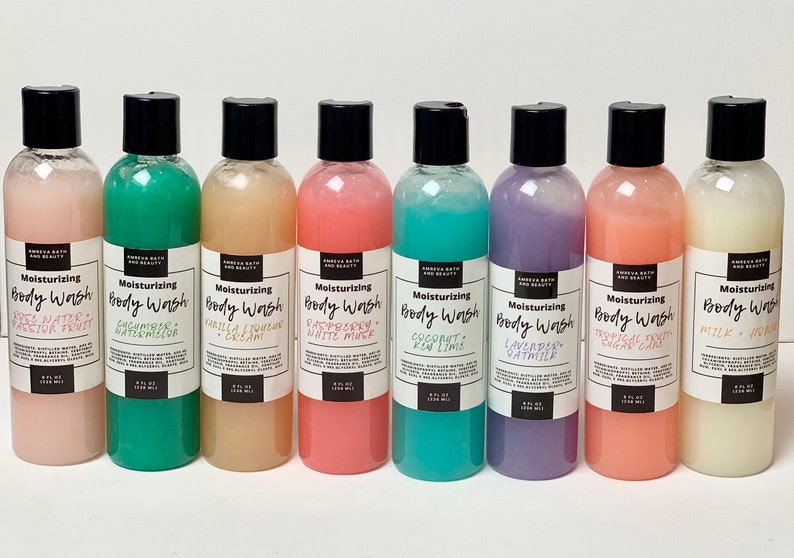 May include: Eight clear plastic bottles of body wash with black lids and labels. The labels have the text "Moisturizing Body Wash" and list different scents, including Rose Water, Cucumber Watermelon, Vanilla &  Liquorice Cream, Raspberry White Mint, Coconut Key Lime, Lavender Oatmilk, Tropical Fruit Sugar Cane, and Milk & Honey.