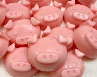 May include: A collection of pink pig-shaped soaps. The soaps are all the same size and shape, and they have a smooth, glossy finish.