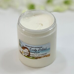May include: A white jar of sugar body polish with a label that reads "Amreva Bath and Beauty Sugar Body Polish Exfoliating Scrub Caribbean Coconut 8 oz / 226g".