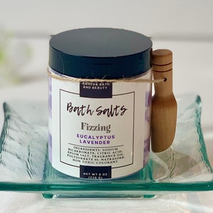 Pode incluir: Um frasco de sais de banho com uma concha de madeira. O frasco &eacute; rotulado como "Bath Salts Fizzing Eucalyptus Lavender" e lista os ingredientes. O frasco est&aacute; sobre um prato de vidro transparente.