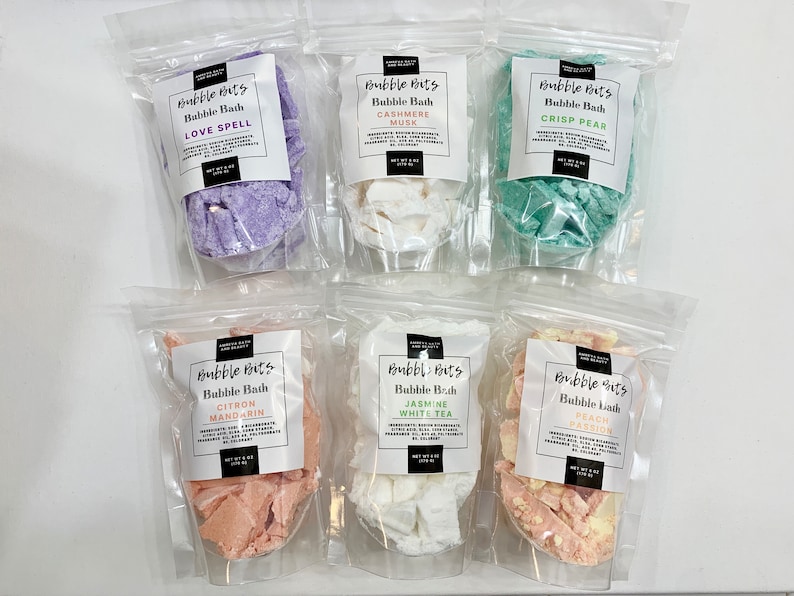 May include: Six clear plastic bags with white labels containing different bath bomb scents. The labels have the text "Bubble Bits" and the scent name. The scents are Love Spell, Cashmere Musk, Crisp Pear, Citron Mandarin, Jasmine White Tea, and Peach Passion.