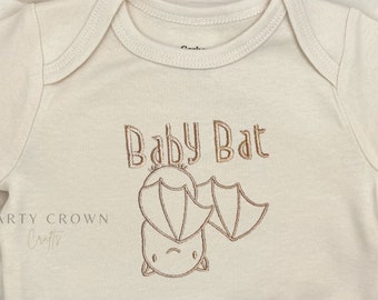 May include: A cream-colored baby onesie with a brown embroidered bat and the text "Baby Bat".