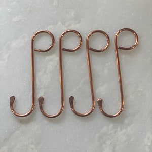 May include: Four copper-colored metal hooks with a rounded top and a pointed bottom. The hooks are arranged in a row, with the rounded tops facing the viewer.