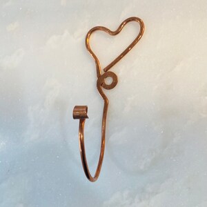 May include: A copper wire heart-shaped hook with a rounded end. The hook is bent into a heart shape with a small loop at the top.