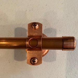 May include: Copper pipe fitting with a copper bracket and two screws. The bracket has the text "242" on it.