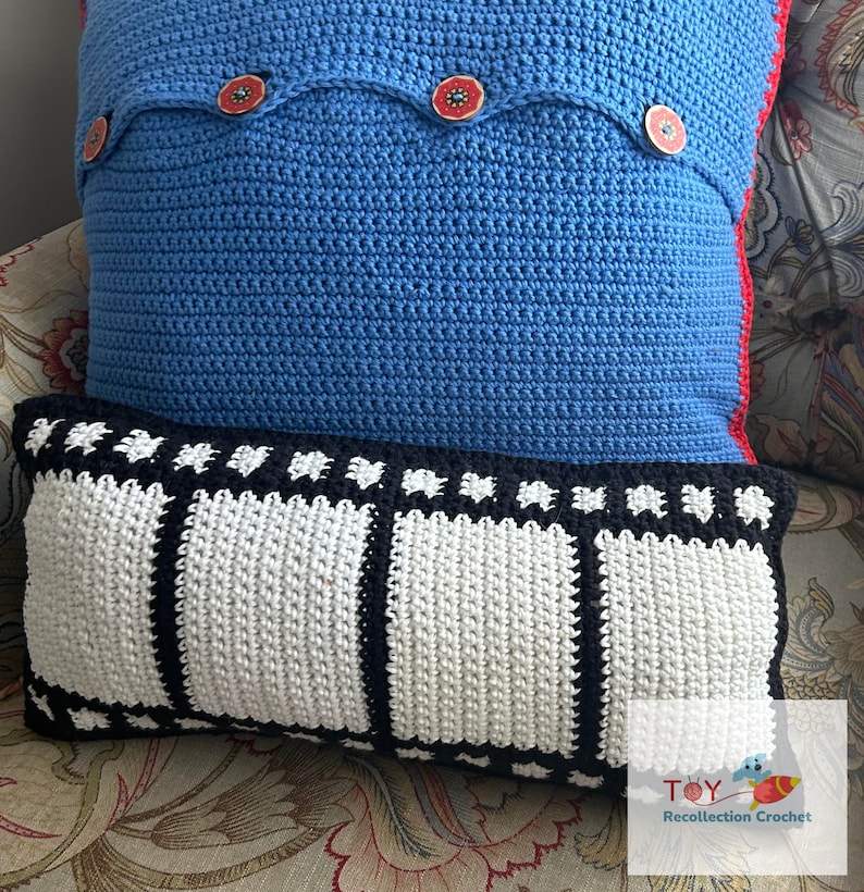 May include: Two crocheted pillows, one blue with red buttons and a white border, and one black and white with a film strip design. The pillows are on a floral patterned couch.