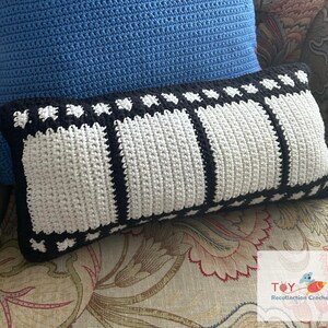 May include: A white and black crochet pillow with a film strip design. The pillow is sitting on a floral patterned couch.