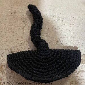 May include: Black crocheted witch hat with a long, curled brim. The hat is made of yarn and has a textured surface.
