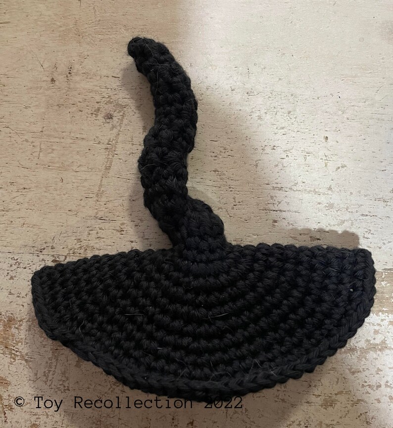 May include: Black crocheted witch hat with a long, curled brim. The hat is made of yarn and has a textured surface.