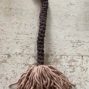 May include: A brown and beige crocheted tassel with a long, brown cord. The tassel is made of a soft, fluffy yarn and would be a great addition to a home decor project.