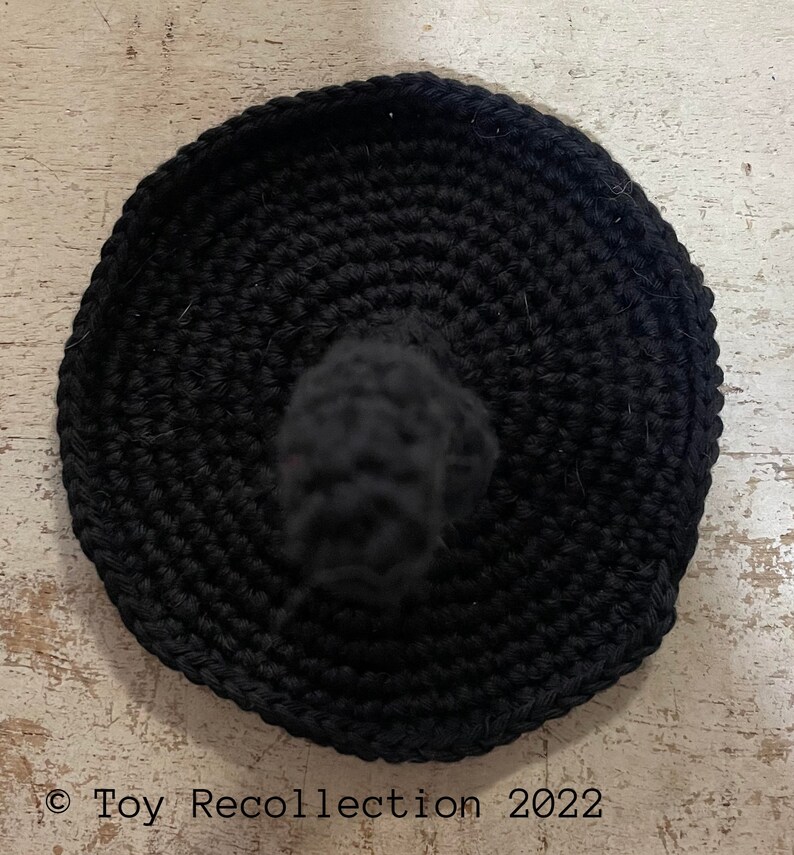 May include: Black crocheted witch hat with a pointed top. The hat is made using single crochet stitches and has a smooth, even texture.