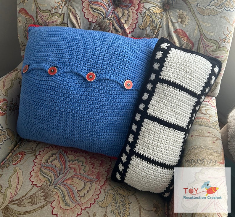 May include: Two crocheted pillows, one blue with red buttons and one black and white with a film strip design. The pillows are on a floral patterned couch.