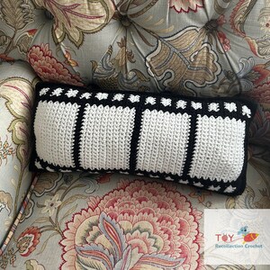 May include: A black and white crocheted pillow with a film strip design. The pillow is sitting on a floral patterned armchair.