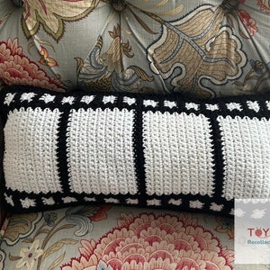 May include: A black and white crocheted pillow with a film strip design. The pillow is sitting on a floral patterned couch.