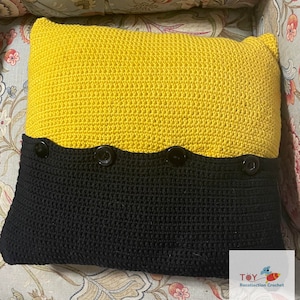 May include: A yellow and black crocheted pillow with four black buttons. The pillow is made with a textured stitch and has a wavy edge.