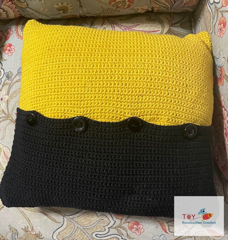May include: A yellow and black crocheted pillow with four black buttons. The pillow is made with a textured stitch and has a wavy edge.